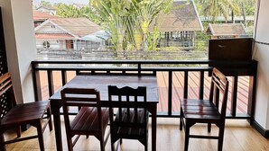 Techo de madera, un balcón con vistas a casas y árboles, y una mesa con sillas.