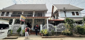 A two-story building with a tiled roof, a gated entrance, and a sign indicating a guest house. - Singharat Guest House (Luang Prabang)