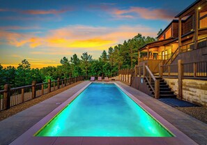 A swimming pool with a wooden deck, a covered outdoor area, and a view of trees and a sunset. - Lux•Insane Views•Sleep 26•Heated Pool•Game Room (Broken Bow)