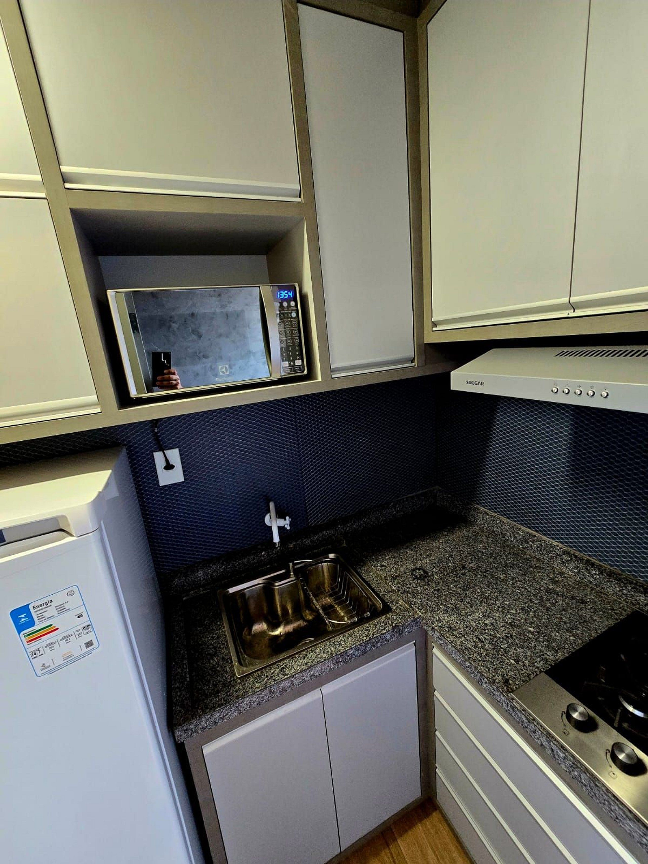 A compact kitchen with a microwave, a stainless steel sink, and a gas stove.