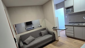 A modern living space with a grey sofa, a flat-screen TV, and a kitchen area with cabinets and a microwave.