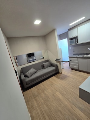 A modern living space with a grey sofa, a flat-screen TV, and a kitchen area with cabinets and a microwave.