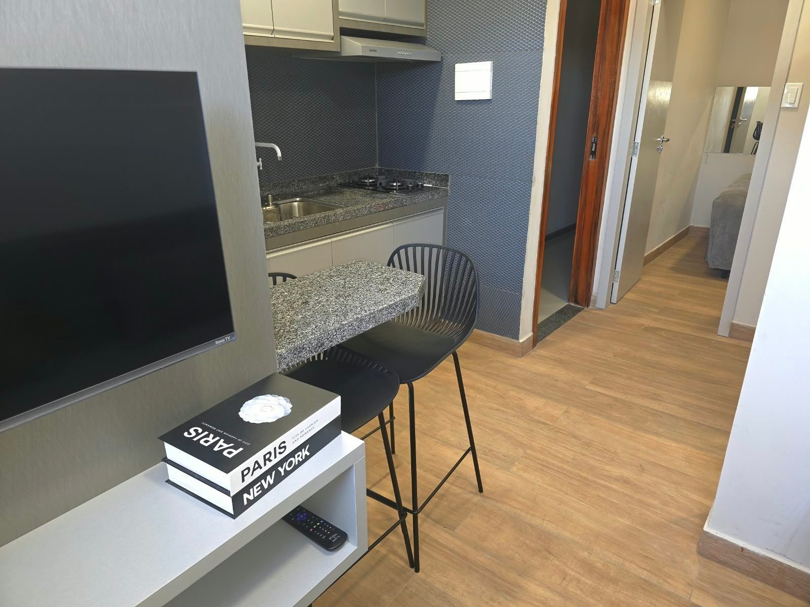 Une cuisine moderne dotée d’une cuisinière intégrée, d’un coin repas avec un tabouret de bar et d’un téléviseur à écran plat posé sur un meuble.