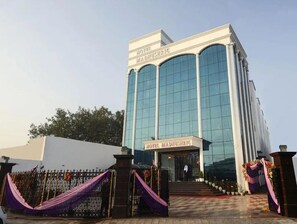 A modern hotel with a glass facade, a prominent entrance, and a name sign. - Hotel Madhushrie (Etmadpur)