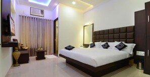 A hotel room with a large bed, a bedside table, a nightstand, a mirror, and a ceiling light. - Hotel Madhushrie (Etmadpur)