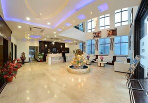 A hotel lobby with a reception desk, seating area, and large windows. - Hotel Madhushrie (Etmadpur)