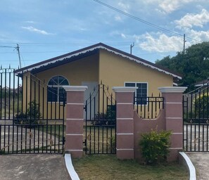 A single-story building with a beige facade, a red roof, and a black metal gate. - 🌴 New Harbour Haven | Spacious Family Retreat in Gated Community (Old Harbour)