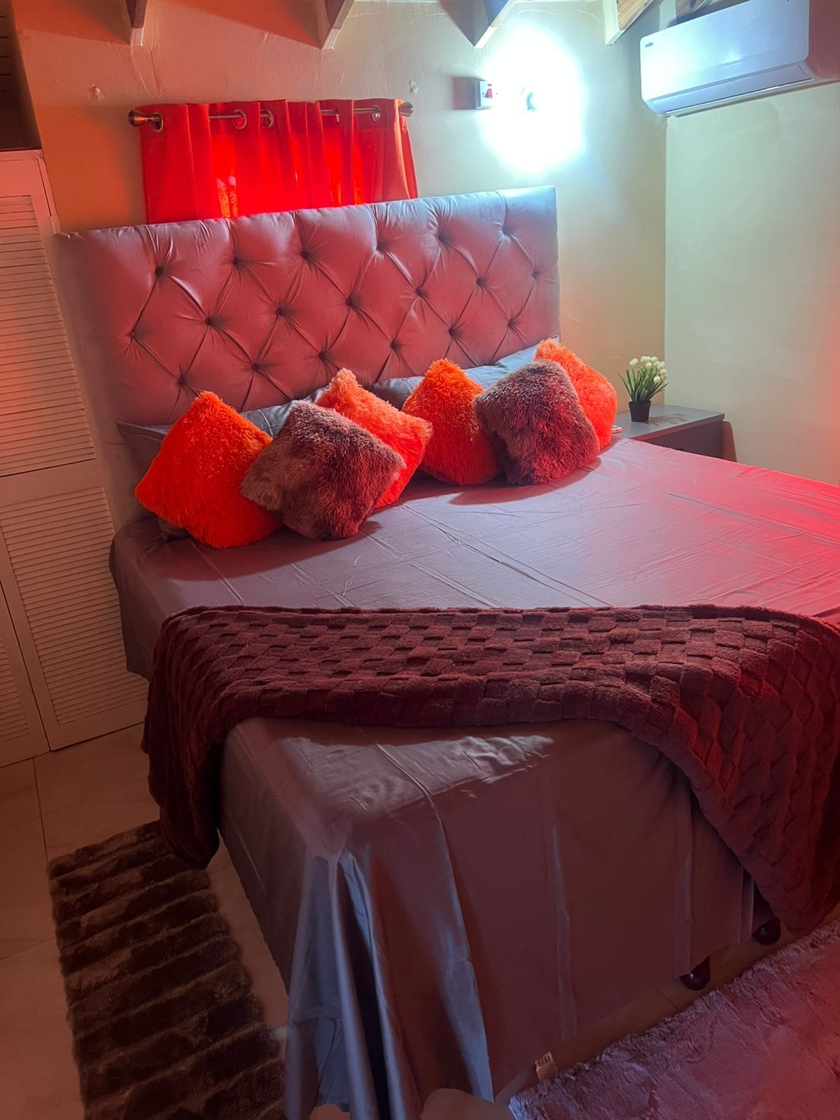 A bedroom with a tufted headboard, a bed with a red blanket, and multiple pillows.