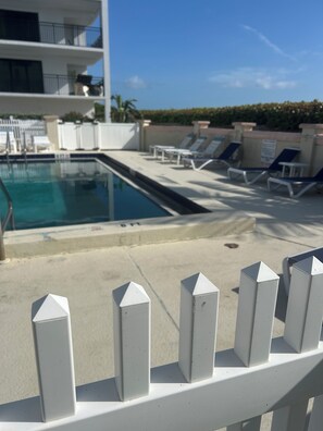 A swimming pool with lounge chairs and a building in the background. - Perfect combination of ocean and sunshine in this 2/2 oceanfront condo (Jensen Beach)