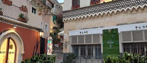 A courtyard with potted plants, outdoor seating, and buildings with balconies and signage.