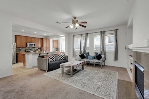 A modern living room with a sofa, coffee table, and a fireplace. There is a kitchen area with wooden cabinets and a microwave.
