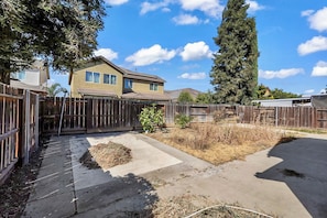 A residential backyard with a wooden fence, a concrete patio, and a house in the background.