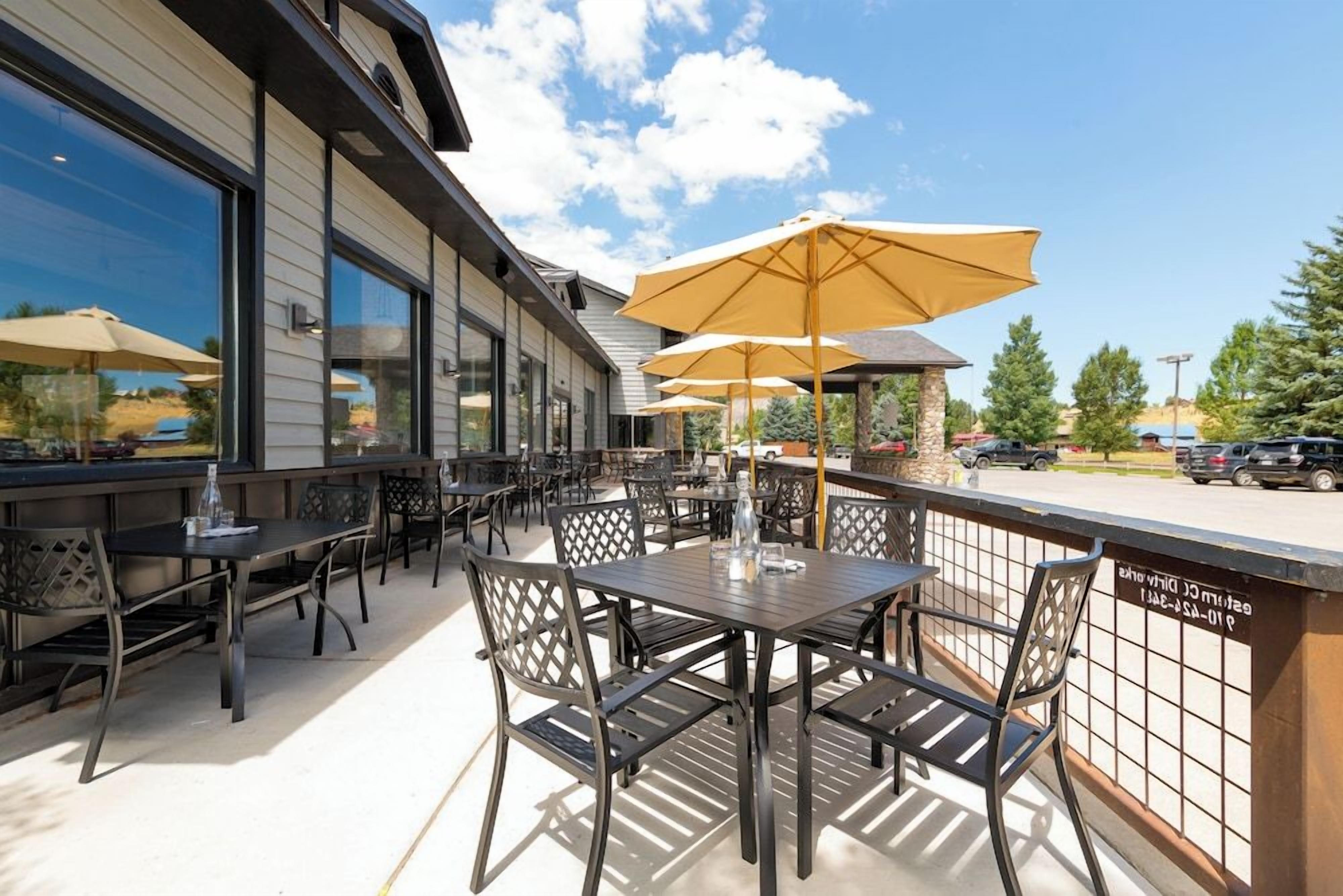 An outdoor patio with tables and chairs, umbrellas, and a view of the parking area.