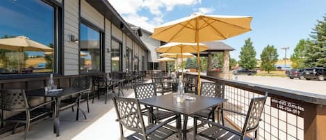 An outdoor patio with tables and chairs, umbrellas, and a view of the parking area.