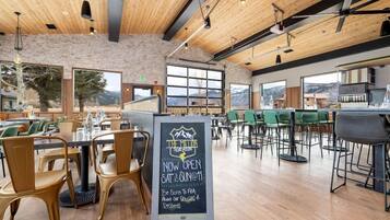 A restaurant interior with wooden ceiling beams, large windows, and a chalkboard sign advertising specials.