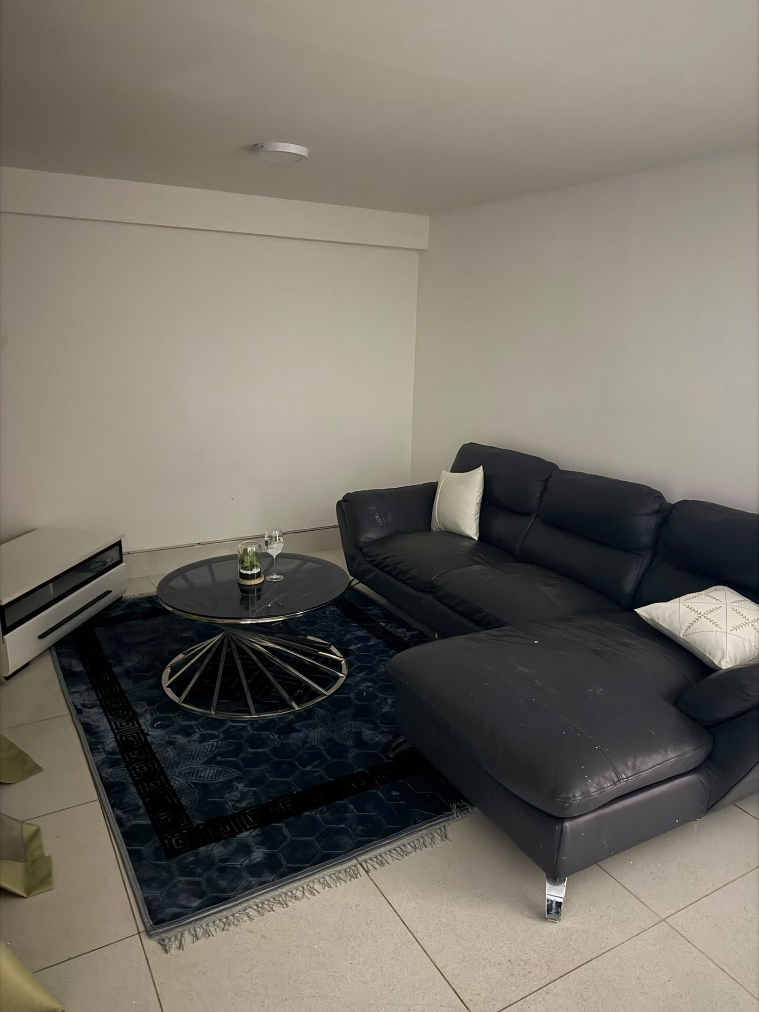 Uma sala de estar moderna com um sofá de couro preto, uma mesa de centro redonda e uma pequena mesa lateral.
