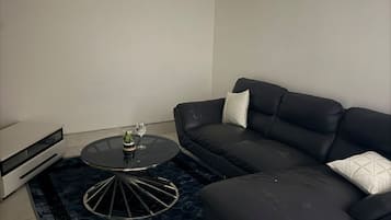 Uma sala de estar moderna com um sofá de couro preto, uma mesa de centro redonda e uma pequena mesa lateral.