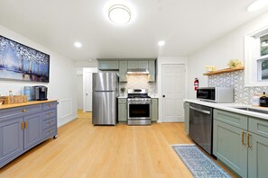 A modern kitchen with stainless steel appliances, grey cabinets, and a wooden floor.