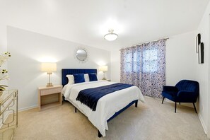 A bedroom with a bed, bedside lamps, a chair, a mirror, and a patterned curtain.