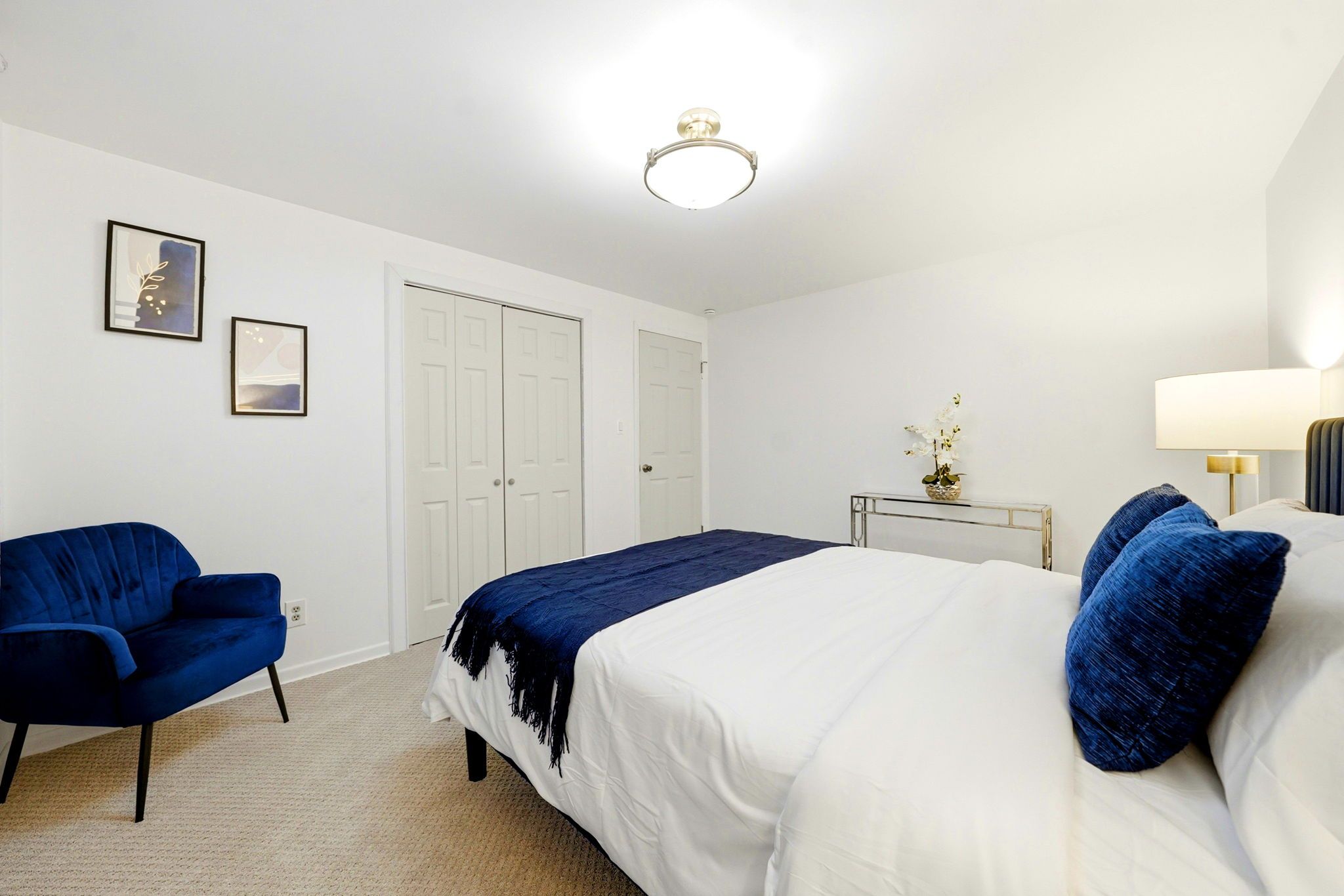 A bedroom with a bed, a chair, a bedside table with a lamp, and two doors.