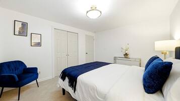 A bedroom with a bed, a chair, a bedside table with a lamp, and two doors.