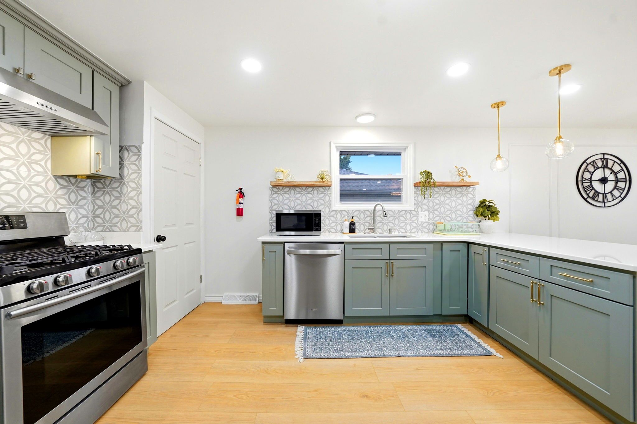 A modern kitchen with stainless steel appliances, light blue cabinets, and a patterned backsplash.