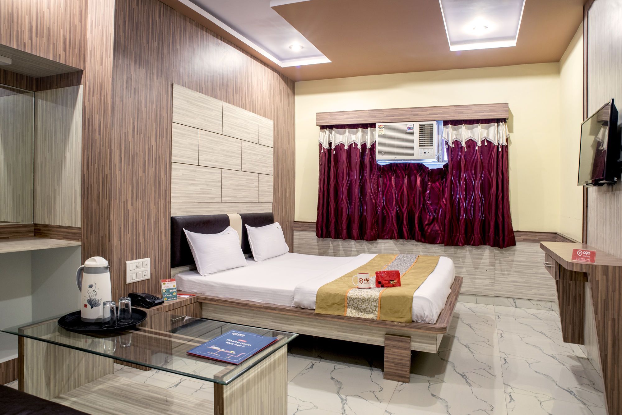 A hotel room with a bed, a glass coffee table, a TV, and a window with curtains.