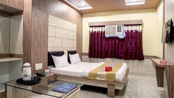 A hotel room with a bed, a glass coffee table, a TV, and a window with curtains.