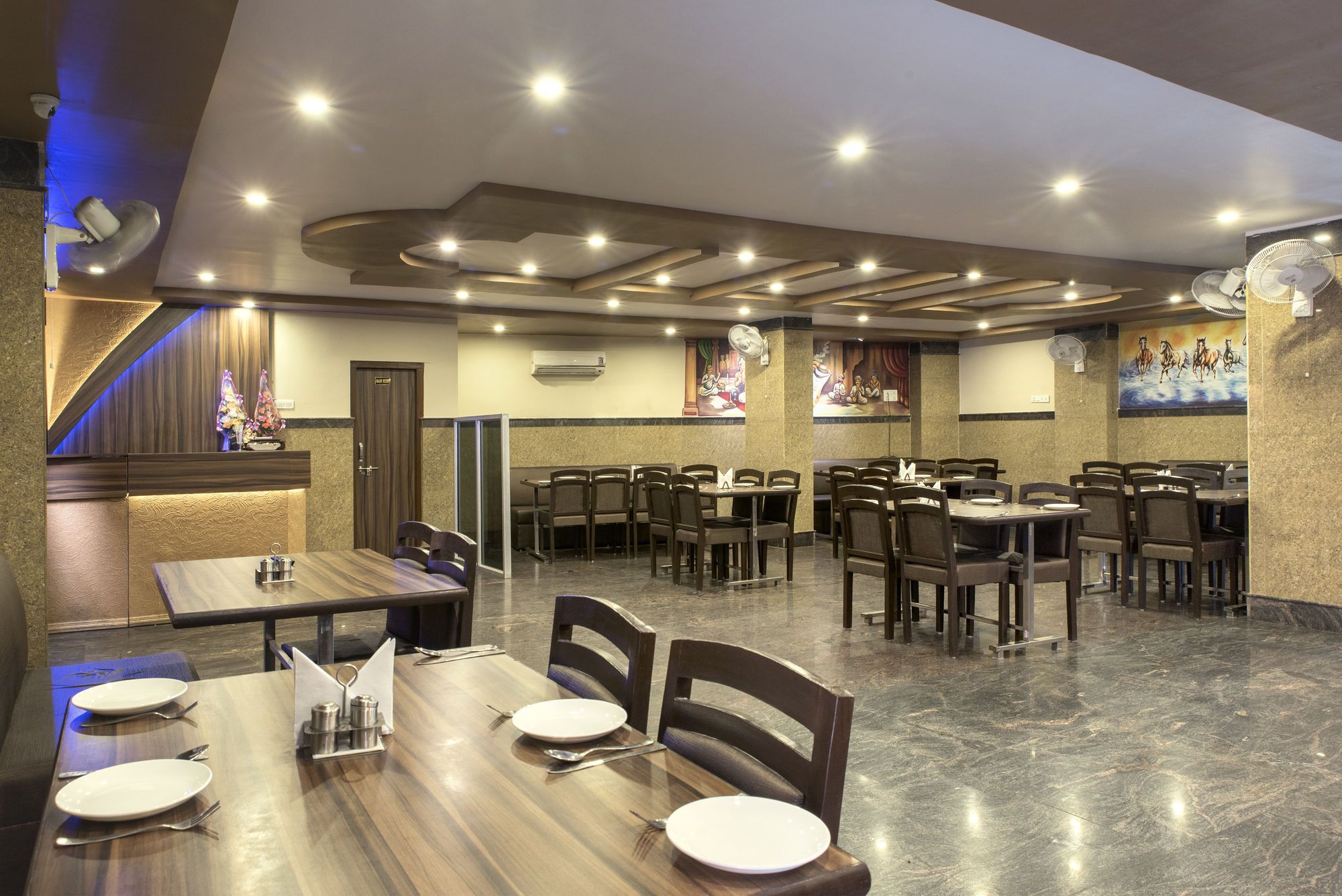 A restaurant with multiple dining tables and chairs, a marble floor, and a ceiling with recessed lighting.