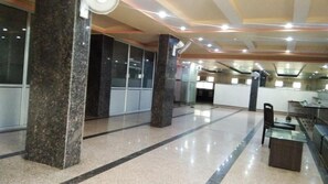 Um hall amplo com colunas de mármore, uma mesa de centro de vidro e um balcão de recepção.