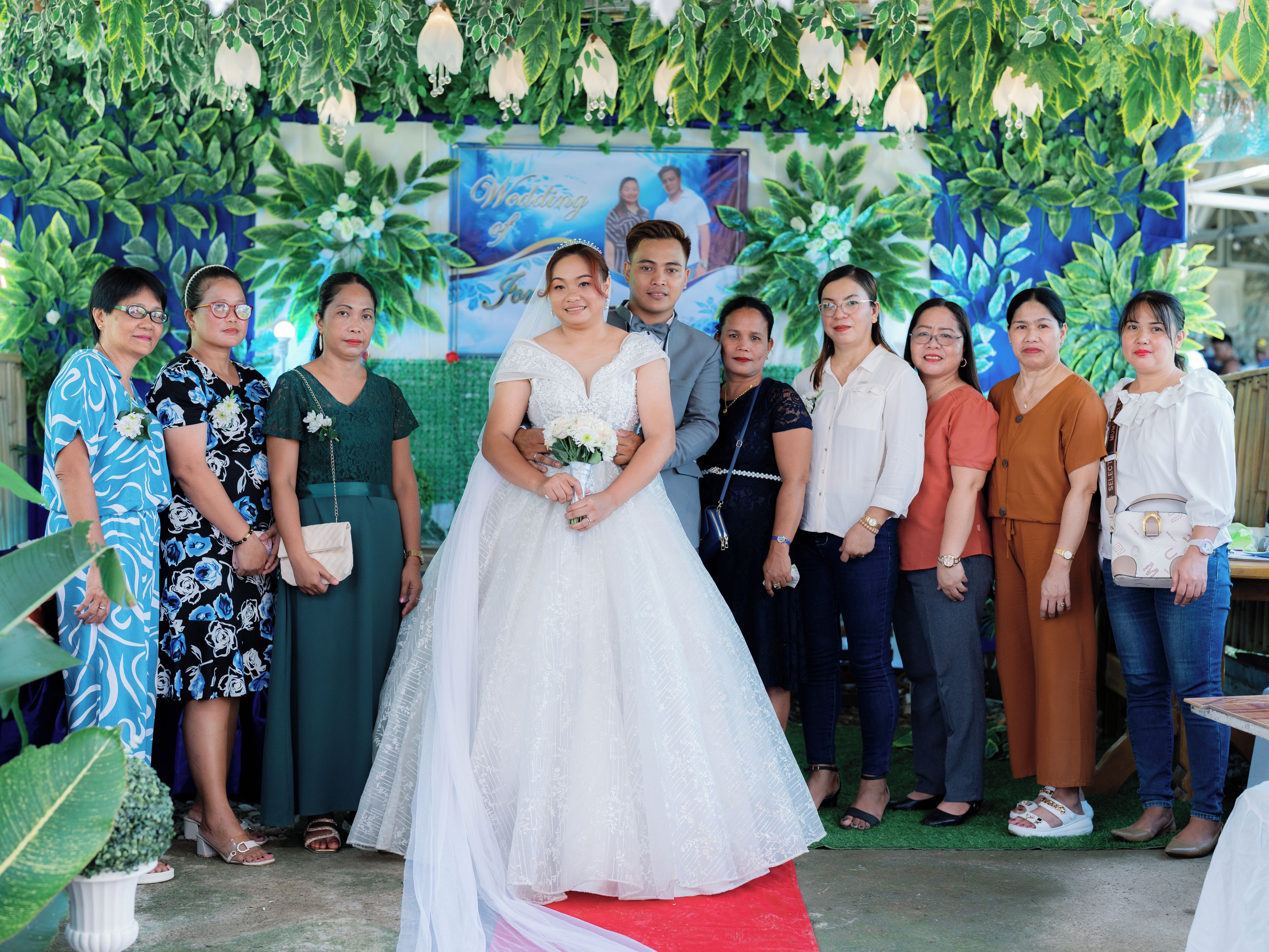 A group of people standing in front of a backdrop with greenery and a wedding theme.