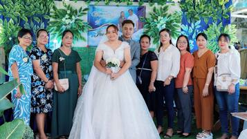 A group of people standing in front of a backdrop with greenery and a wedding theme.