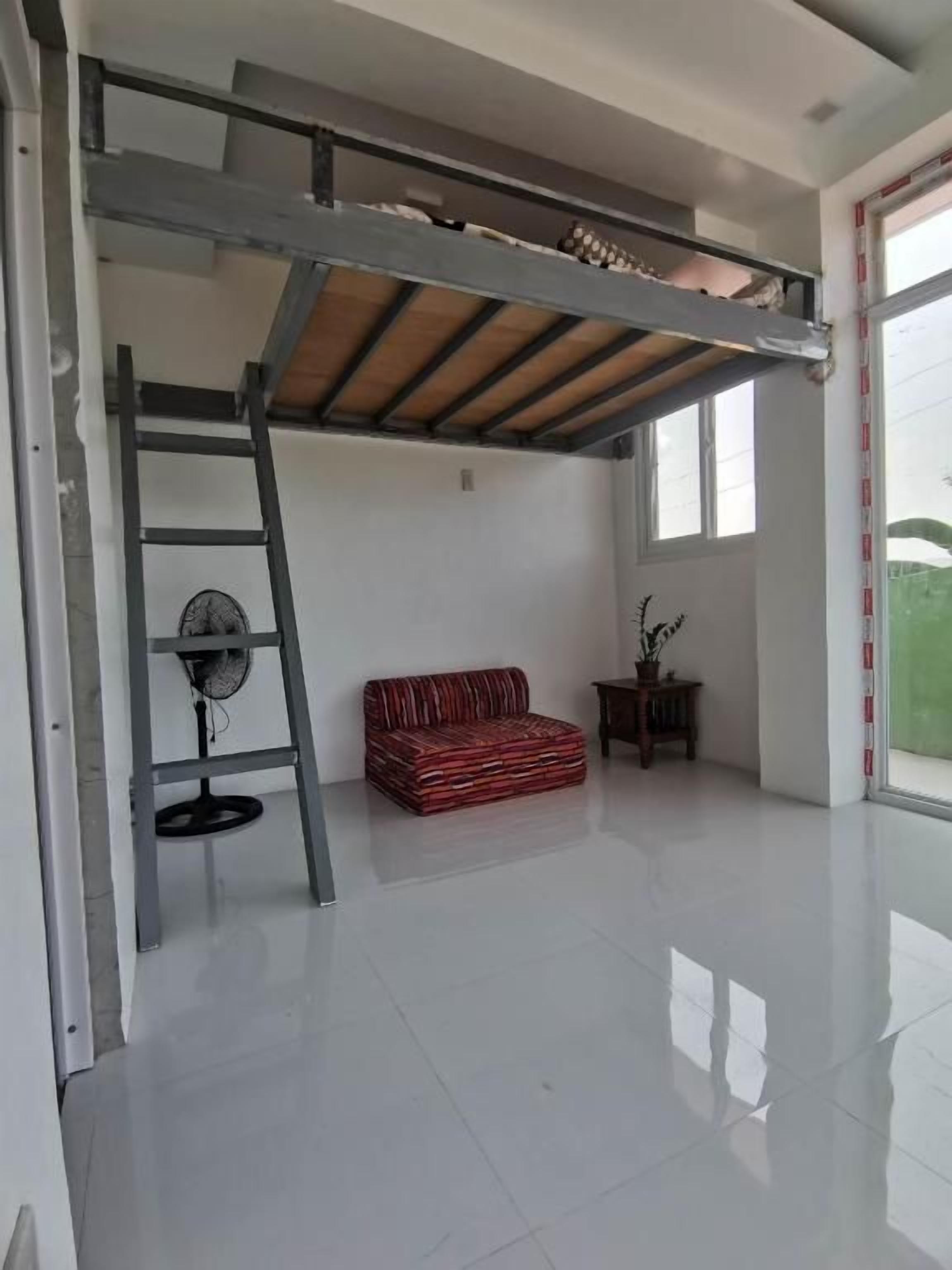 Una habitación con cama tipo litera, ventilador, sofá rojo y ventana.