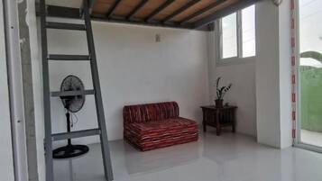 Una habitación con cama tipo litera, ventilador, sofá rojo y ventana.