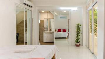 A modern bedroom with a bed, a bathroom with a sink, and a potted plant.