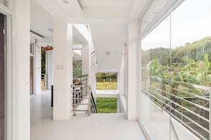 A modern interior with a staircase leading to a balcony overlooking a lush landscape.