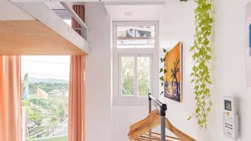 A room with a bed, a window, a drying rack, and a wall-mounted telephone.