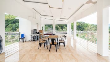 A spacious room with a wooden table and chairs, a computer, and a view of greenery.