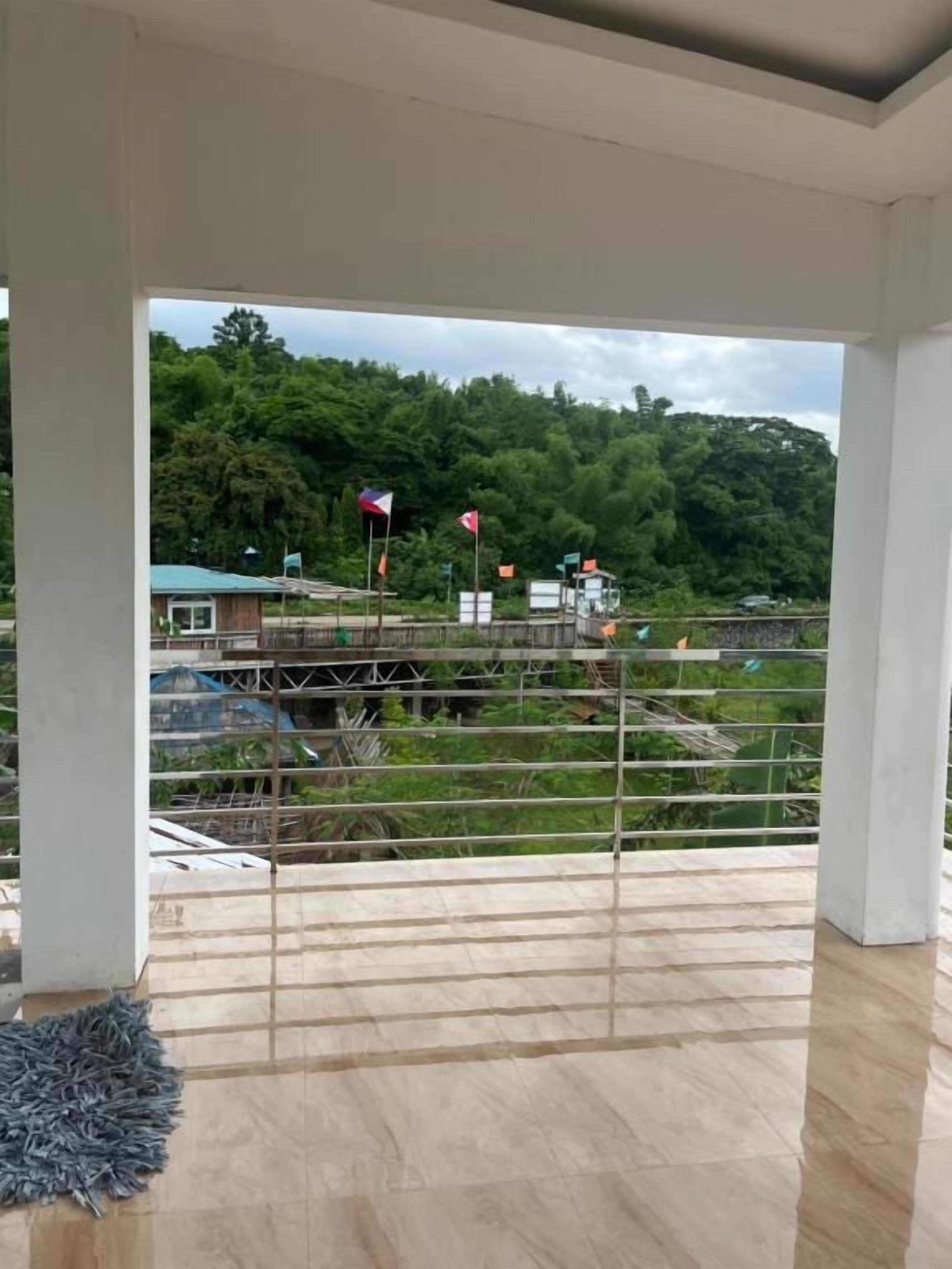 A covered outdoor area with a view of a forested hill and a building with flags.