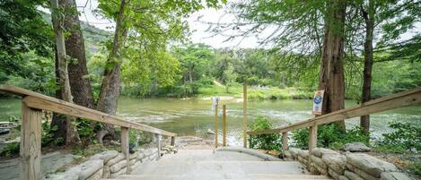 A wooden staircase leading down to a river, surrounded by trees and a stone wall.