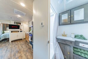Un espace de vie compact comprenant un coin cuisine, un téléviseur diffusant du contenu « NETFLIX » et un lit recouvert d’une couverture bleue.