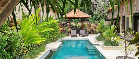 A swimming pool with lounge chairs and a gazebo surrounded by lush tropical plants.
