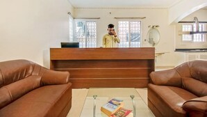 A reception area with a wooden desk, two leather sofas, and a glass coffee table with books. - OYO Rooms Marathahalli Junction (Bengaluru)