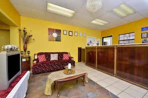 A reception area with a red sofa, a wooden reception desk, and a television. - Americas Best Value Inn & Suites - Russellville (Russellville)