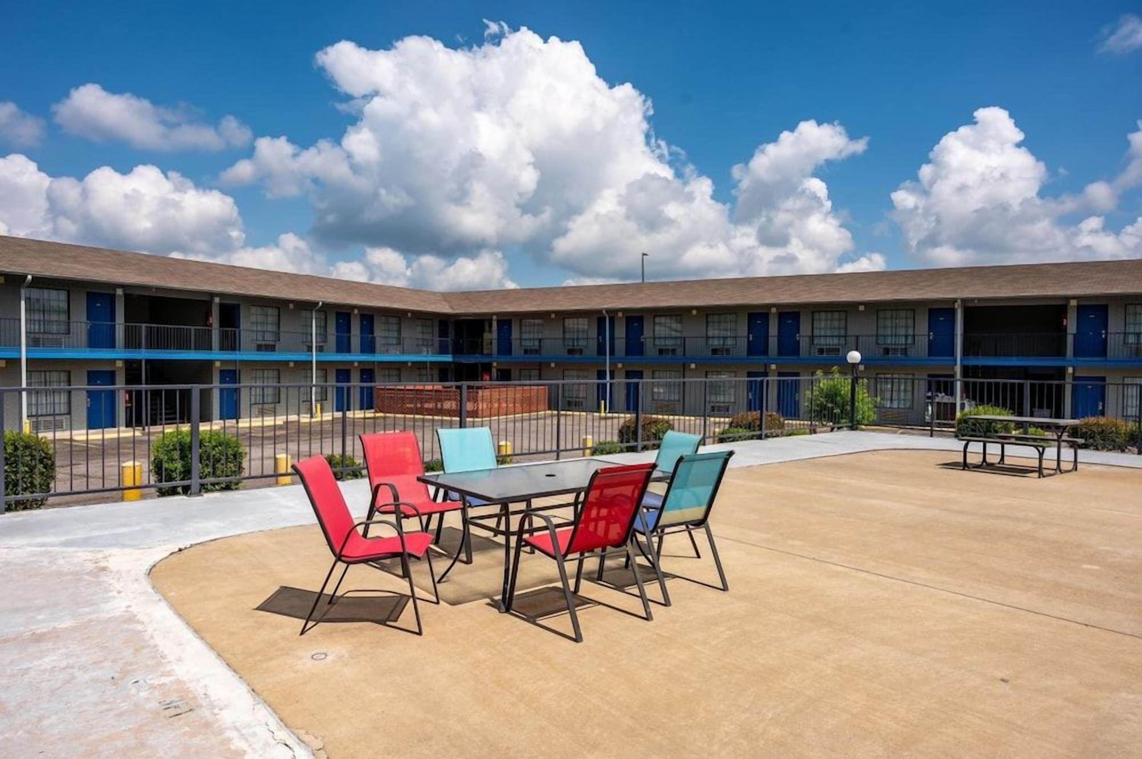 A motel with a courtyard featuring outdoor seating and a fenced area.