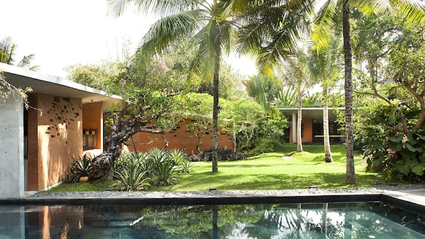 A swimming pool with a clear view of the surrounding garden and a modern building with a unique facade. - Umah Tampih Villa (Ubud)