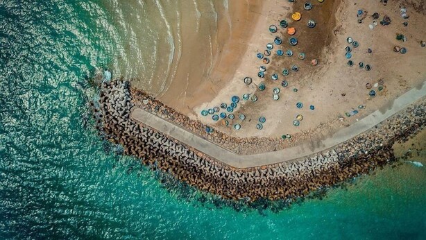 An aerial view of a coastal area with a sandy beach, a rocky breakwater, and scattered objects. - Villa Panda (Phu Thuy)