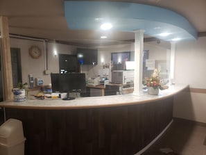 A reception desk with a computer, a clock, and a plant. - Americas Best Value Inn Burlington (Burlington)