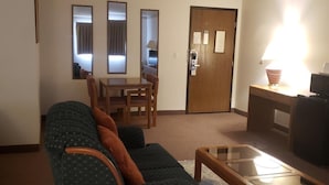 Una sala de estar con sofá, una mesa de centro de vidrio, una mesa de comedor con sillas y una puerta con lector de tarjeta.