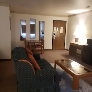 Uma sala de estar com sofá, mesa de centro de vidro, mesa de jantar com cadeiras e uma porta com leitor de cartão-chave.